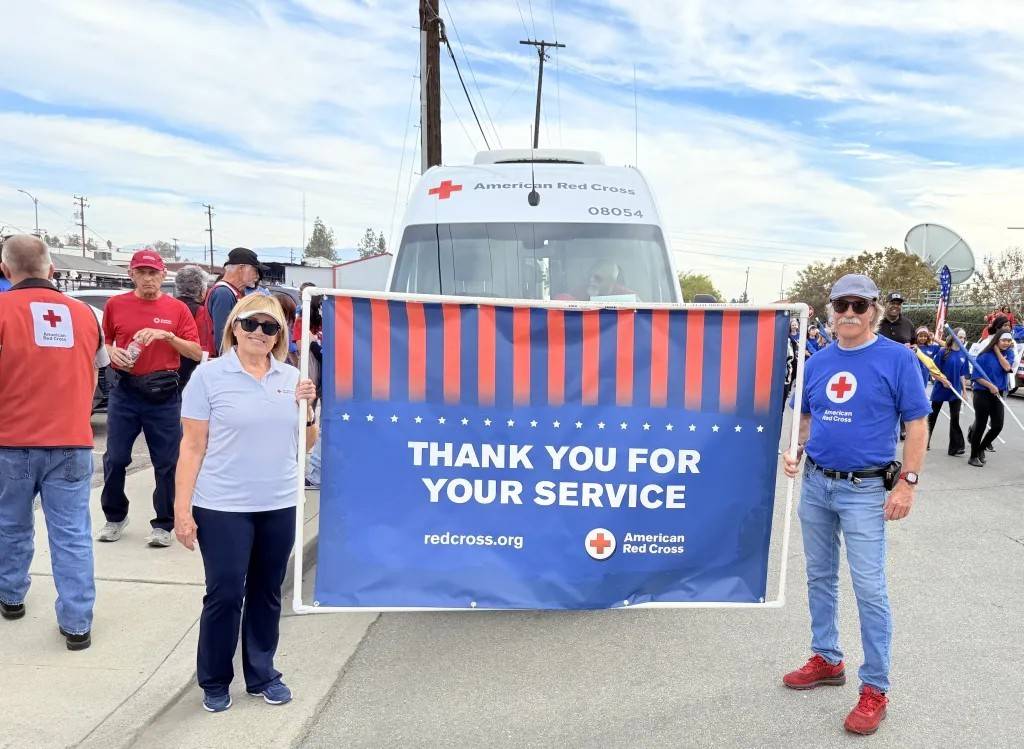 Man and woman in Red Cross shirts hold banner that says "Thank you for your service."