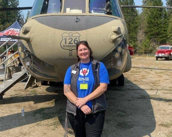 Woman in Red Cross shirt stands in front of helicopter