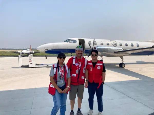 Three Red Cross volunteers stand in front of small plane