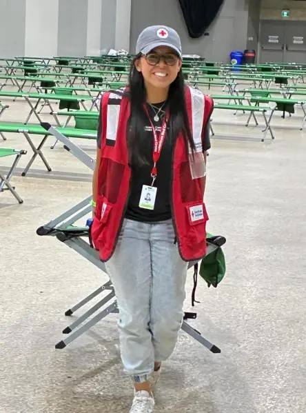 Red Cross volunteer stands in shelter in front of cots