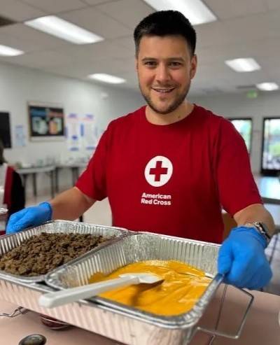 Man in Red Cross shirt holds tin pans of food