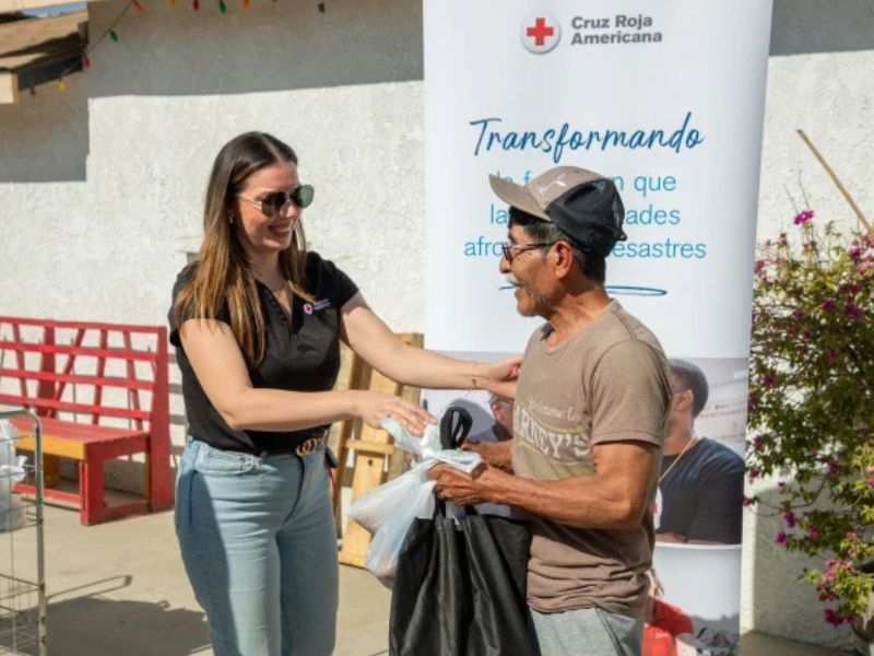 woman speaking with man in front of red cross banner