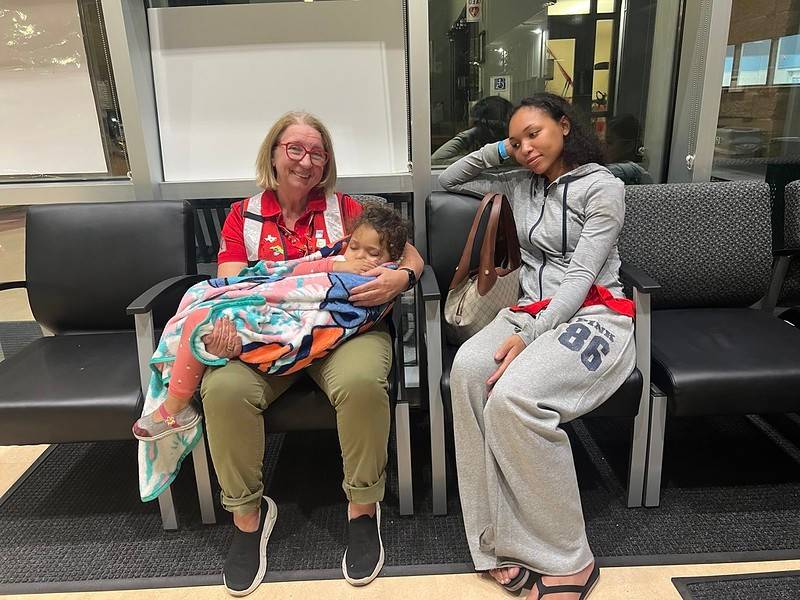 Red Cross volunteer holds young child while mother looks on