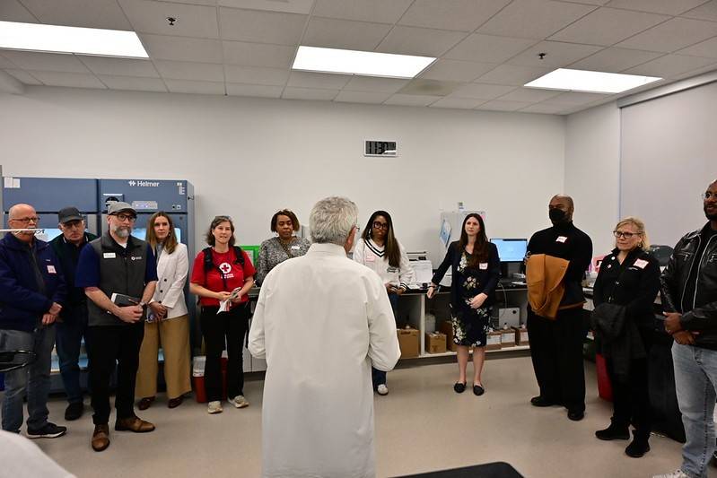 Group of people look to man in white lab coat during blood lab tour