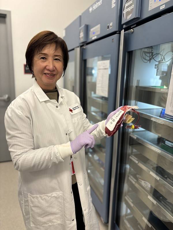 Woman in white lab coat holds bag of donated blood