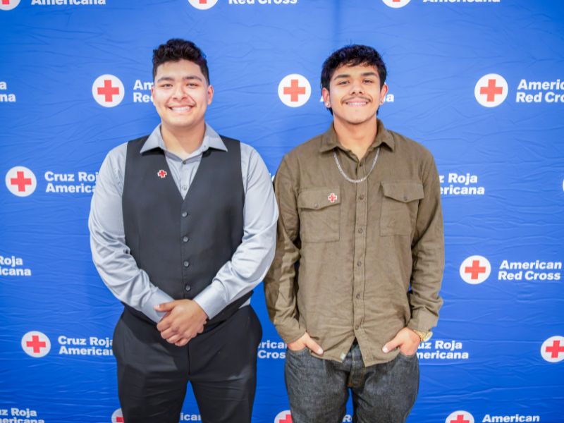 two young people in front of red cross backdrop