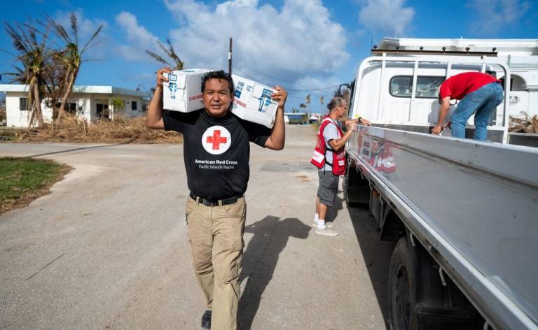 Man in Red Cross shirt carries boxes of relief supplies on his shoulders