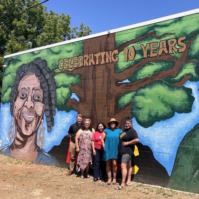 five people stand in front of mural