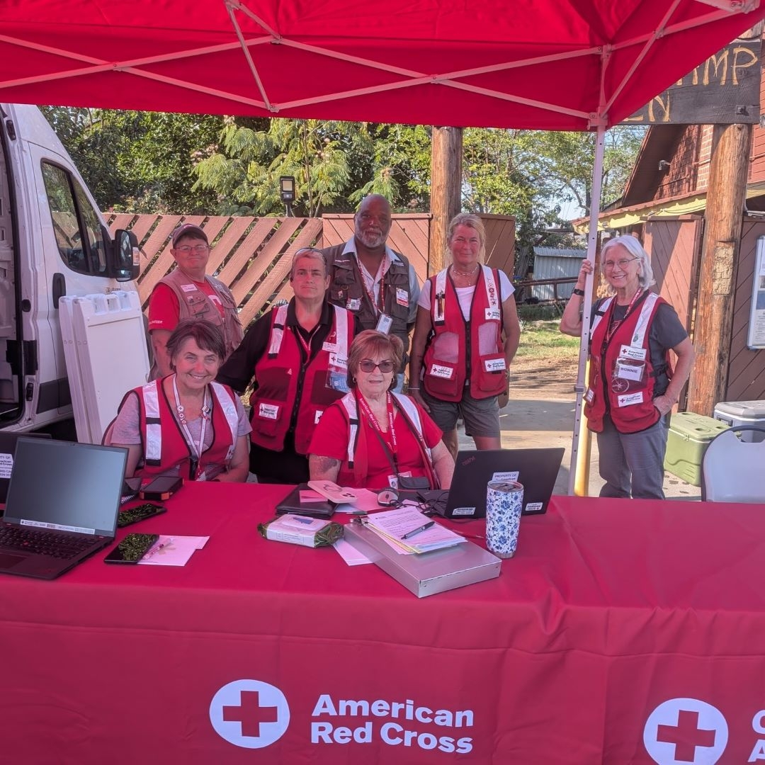 red cross volunteers in vests behind table with red cross logo