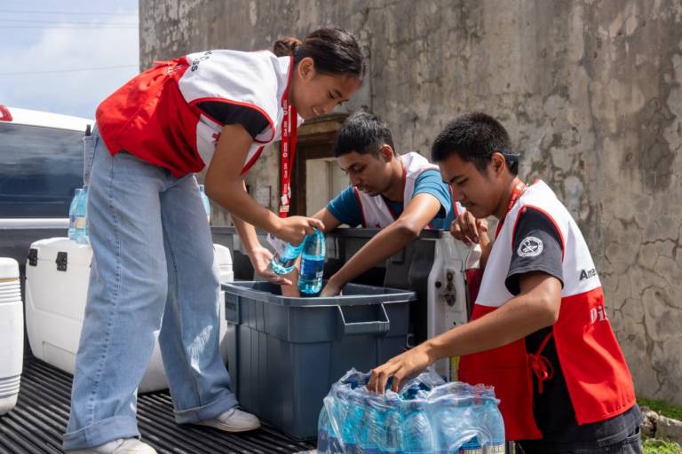 Three young red cross volunteers unload water in back of truck