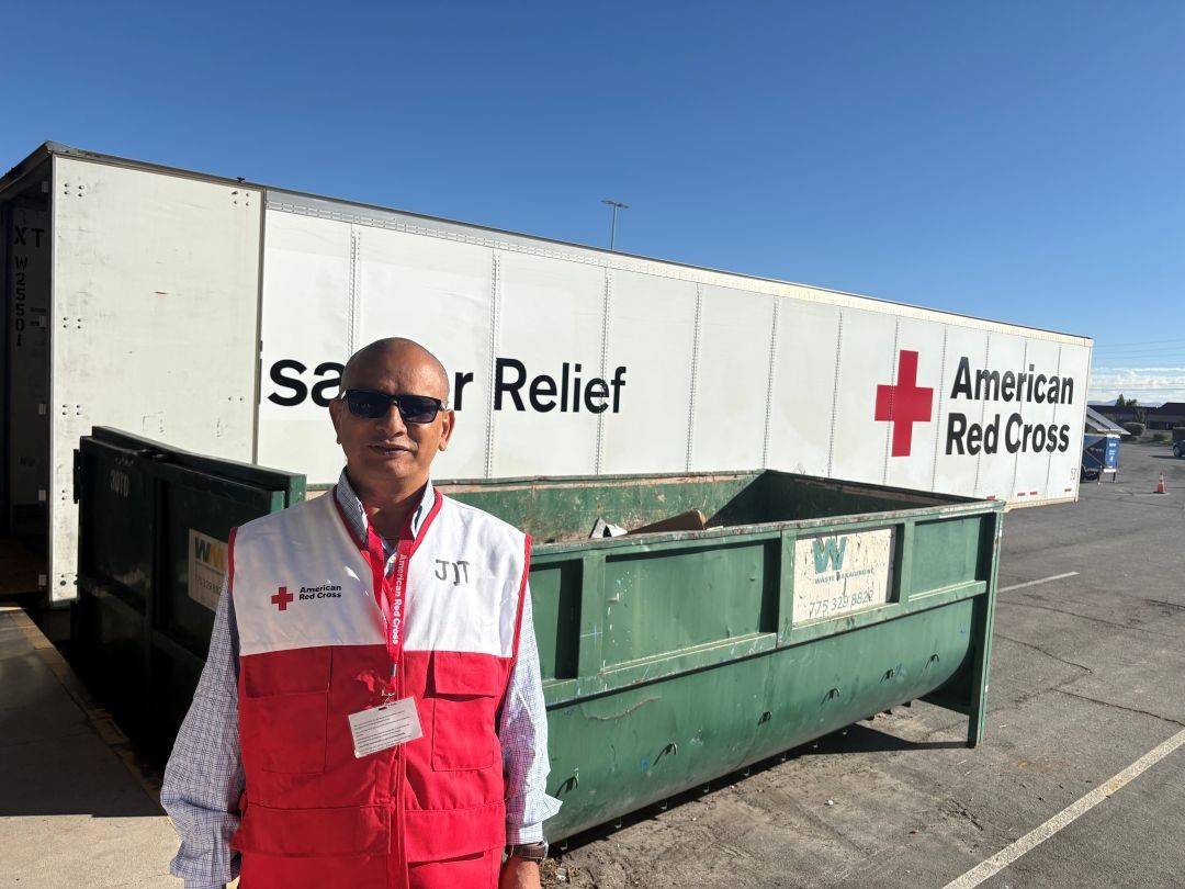 Man in Red Cross vest stands in front of disaster relief truck
