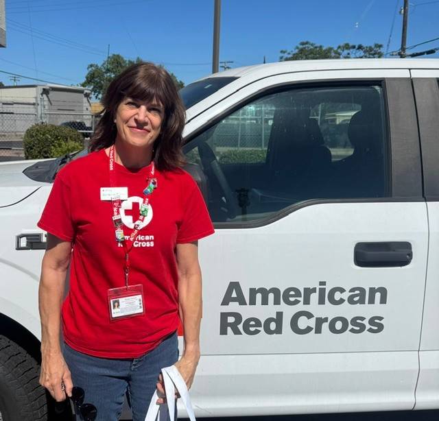 Woman in red cross tshirt stands in front of red cross vehicle