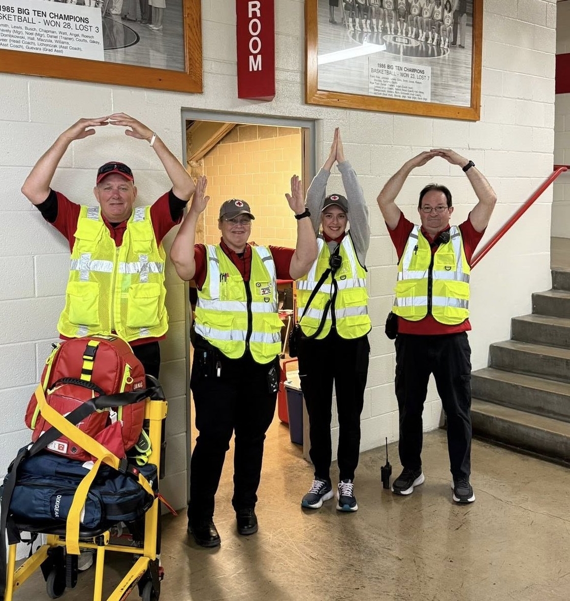 Red Cross volunteers wearing reflective vests standing next to ohio state university brutus buckeye mascot inside ohio state university basketball court.