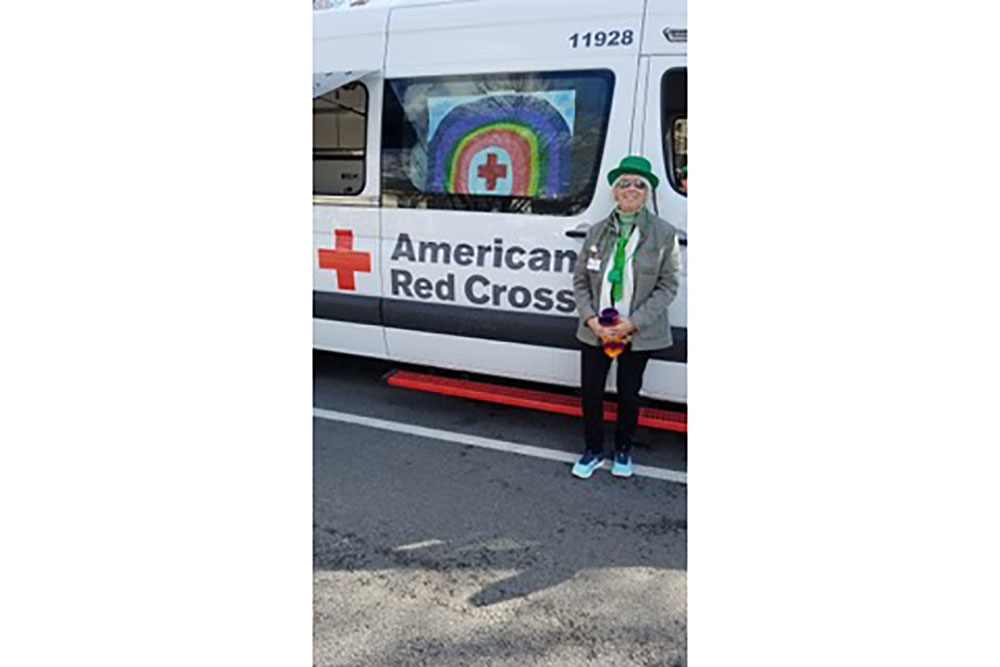 Deb Colvin wearing a green hat and tie while next to a Red Cross van.