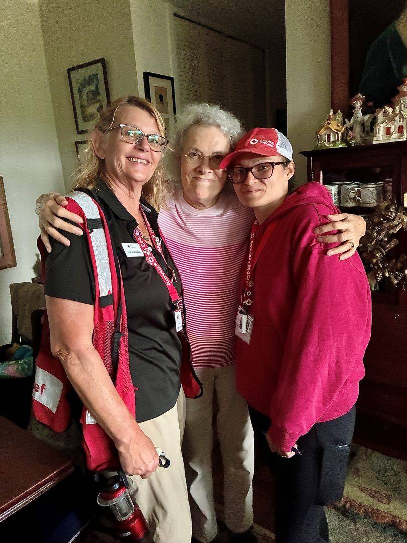 Woman hugs two Red Cross volunteers close inside her home