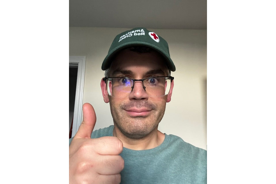 Jamie Quaranta wearing a Red Cross hat and glasses gives a thumbs up.