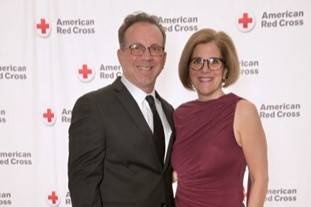Man and woman stand in front of Red Cross back drop