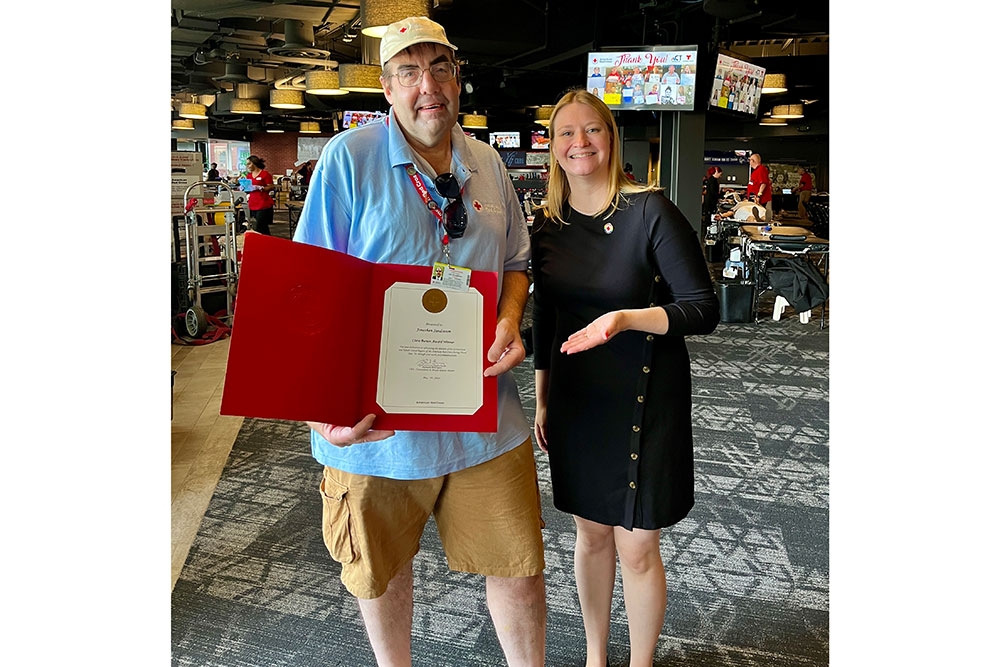 Jonathan Sandstrom holding a Red Cross award with a Red Cross staff member standing next to him.