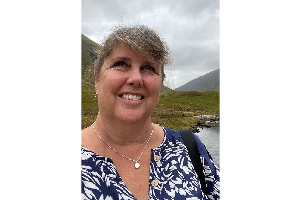 Nancy Perrotti smiling with mountains and a cloudy sky in the background.