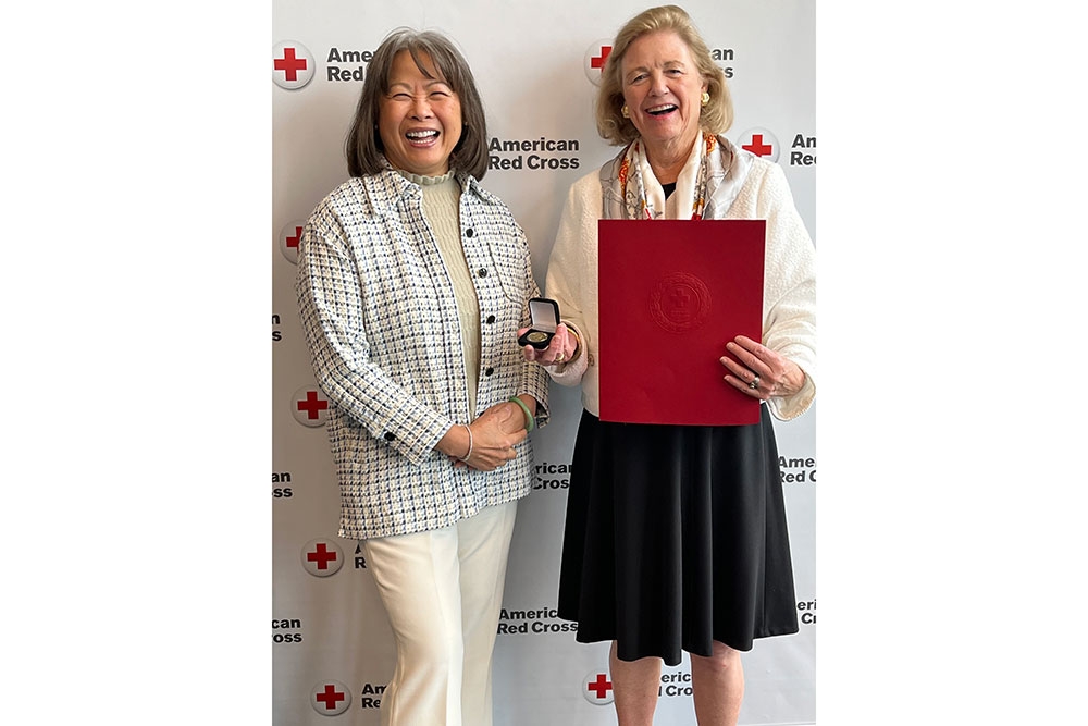 two women, one holding a Red Cross award, stand next to each other at a Red Cross event.