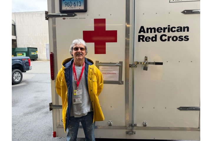 Paul Stranieri in a rain coat standing next to a Red Cross storage container.