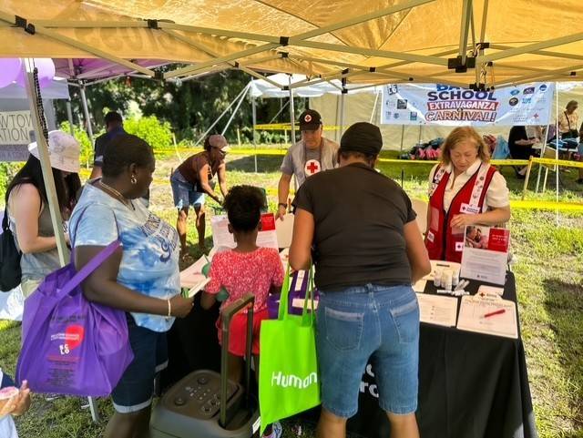 Red Cross volunteers stand under tent handing out supplies to families