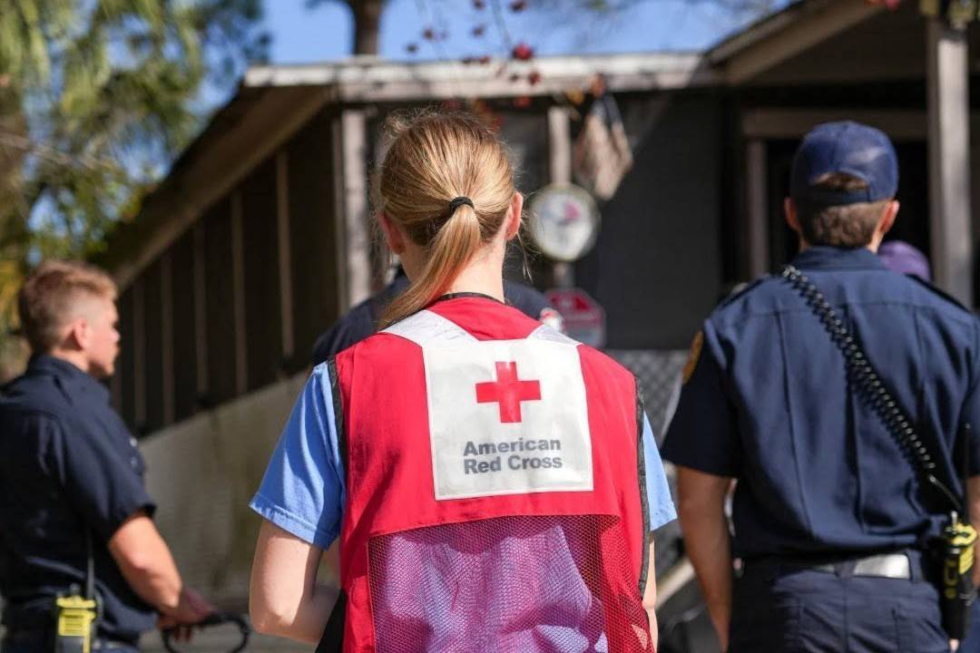 Woman stands outside with back to camera in Red Cross vest 