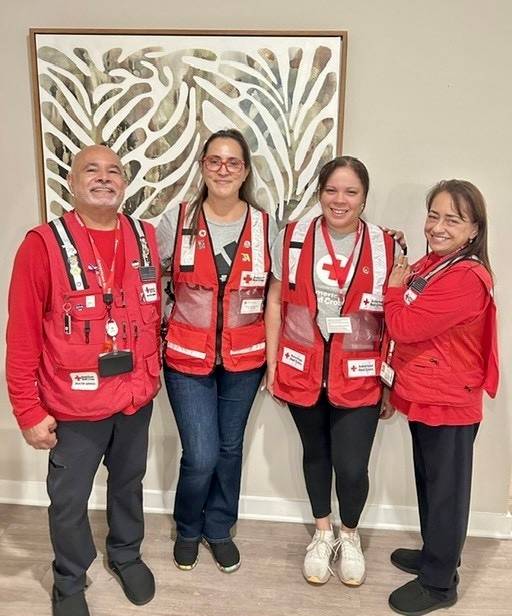Group of four Red Cross volunteers stand next to one another inside building