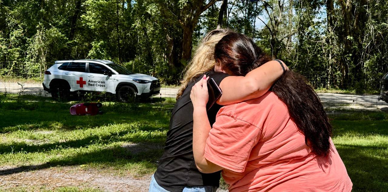 Two women hug with Red Cross car in background
