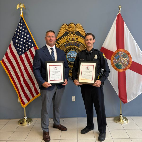 two men stand with red cross awards in front of flags