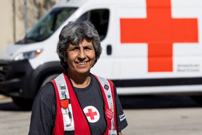 red cross volunteer red cross vest with a red cross vehicle parked in the background.