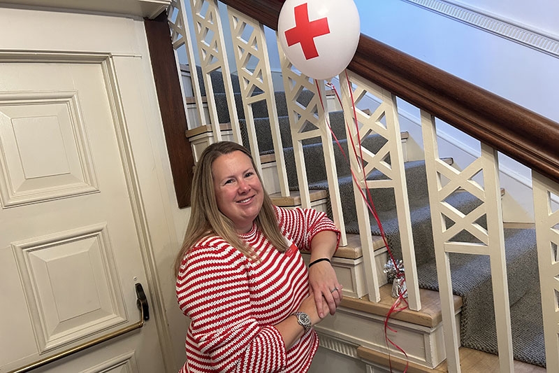 Christine Quinn leaning on a staircase that has a Red Cross balloon tied to a weight.