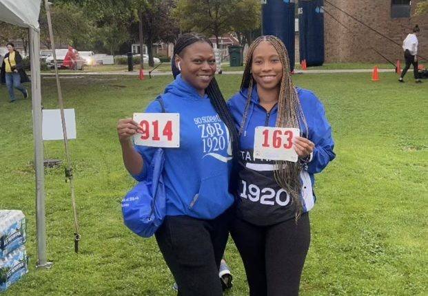 Two women stand outside holding numbered bibs