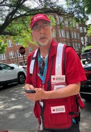 Man wears Red Cross vest while on his phone