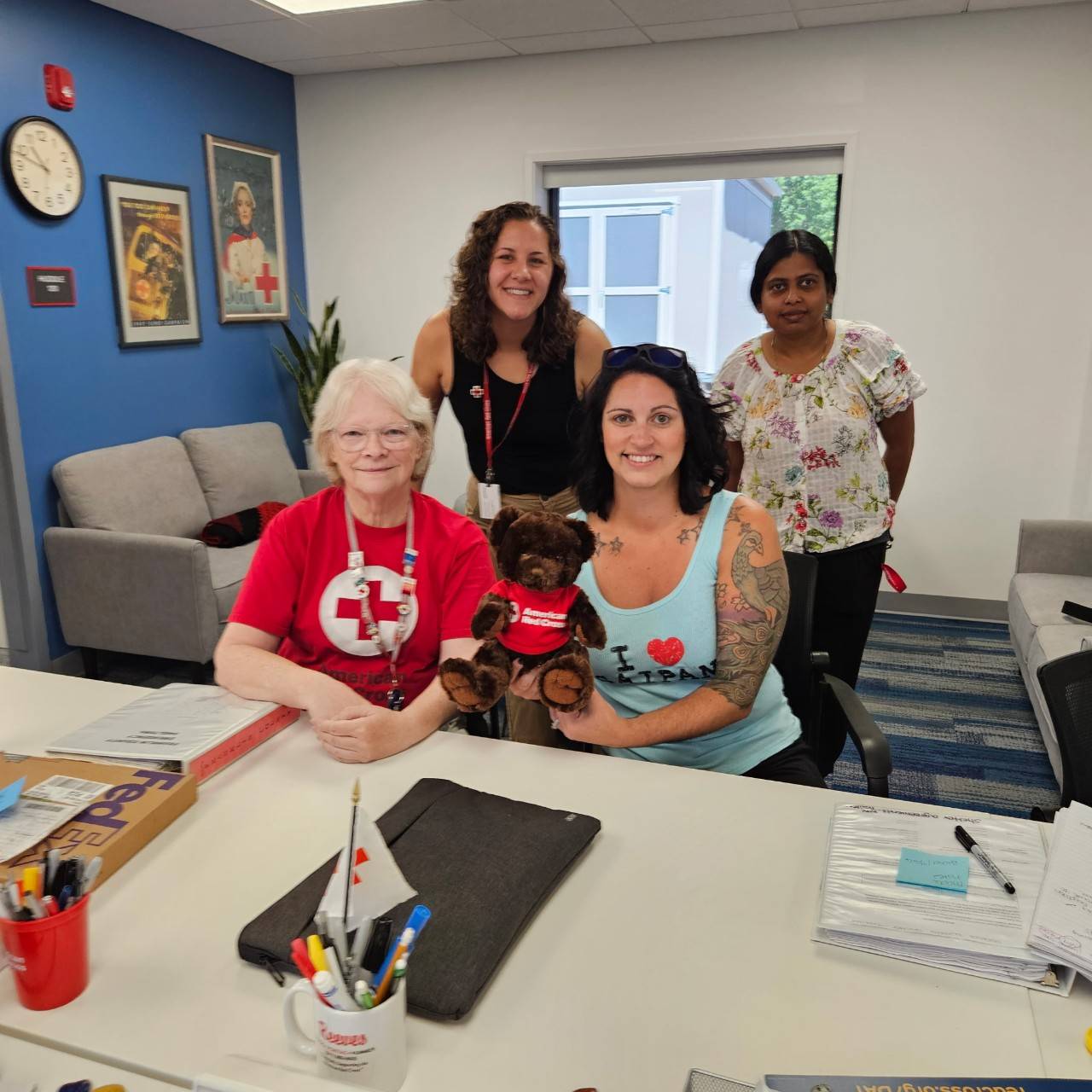 Group of people sit behind table and hold small stuffed bear