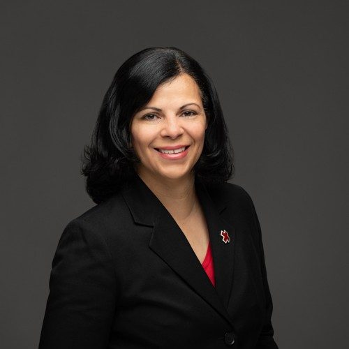woman in red shirt and black blazer with a red cross pin