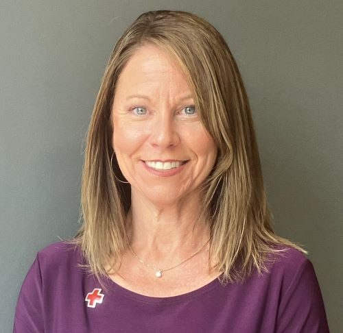 woman smiling in purple sweater with red cross pin