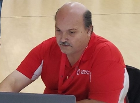 a red cross volunteers at a table in front of a computer.