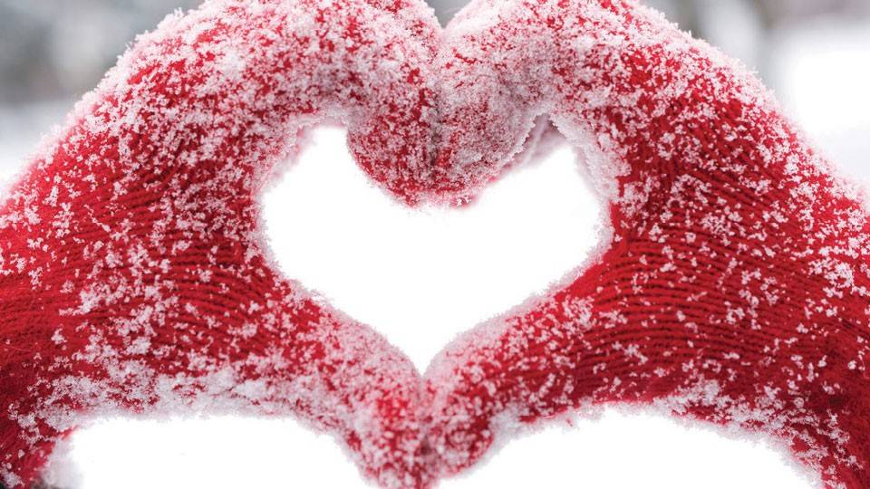 two hands in red mittens covered in snow make a heart shape.