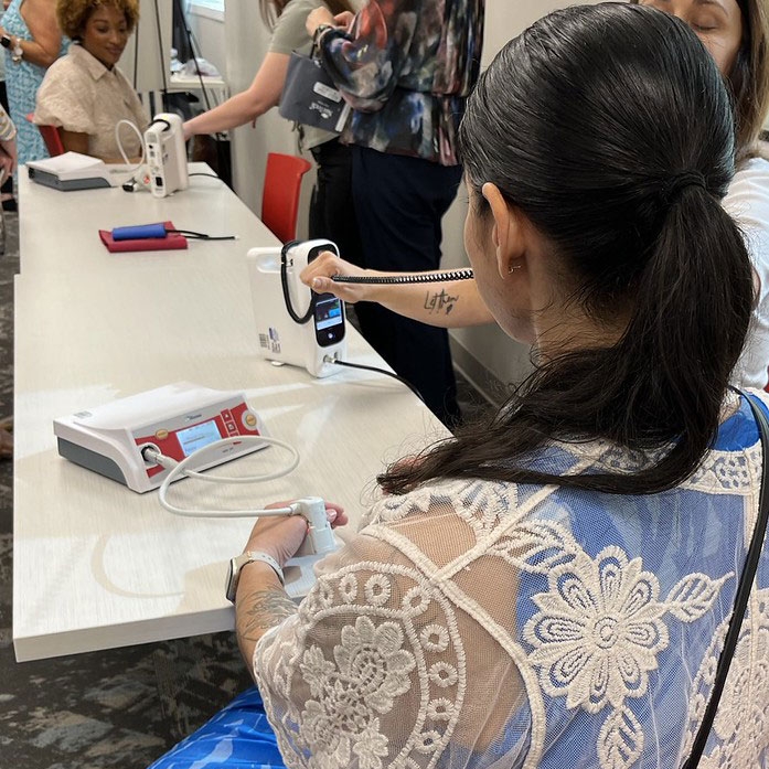 a woman sitting at a table with other women testing the non-invasive hemoglobin device used before a blood donation.