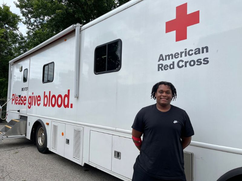 young man smiling in front of red cross blood mobile