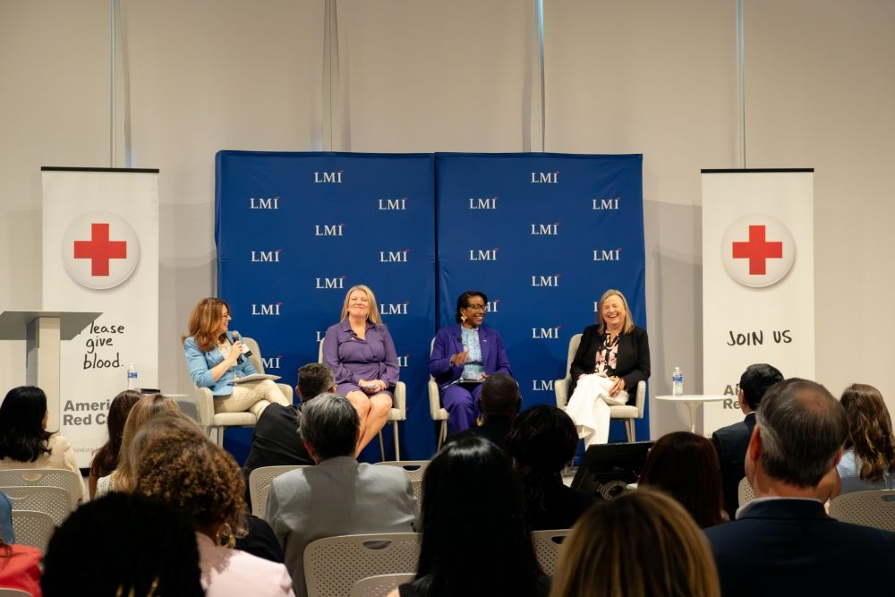Four women sitting on a stage on a panel talking to an audience.