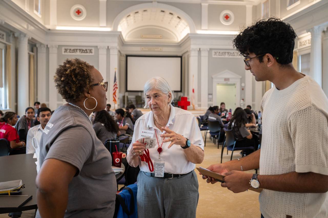 Woman stands inside national Red Cross office building speaking with two other people