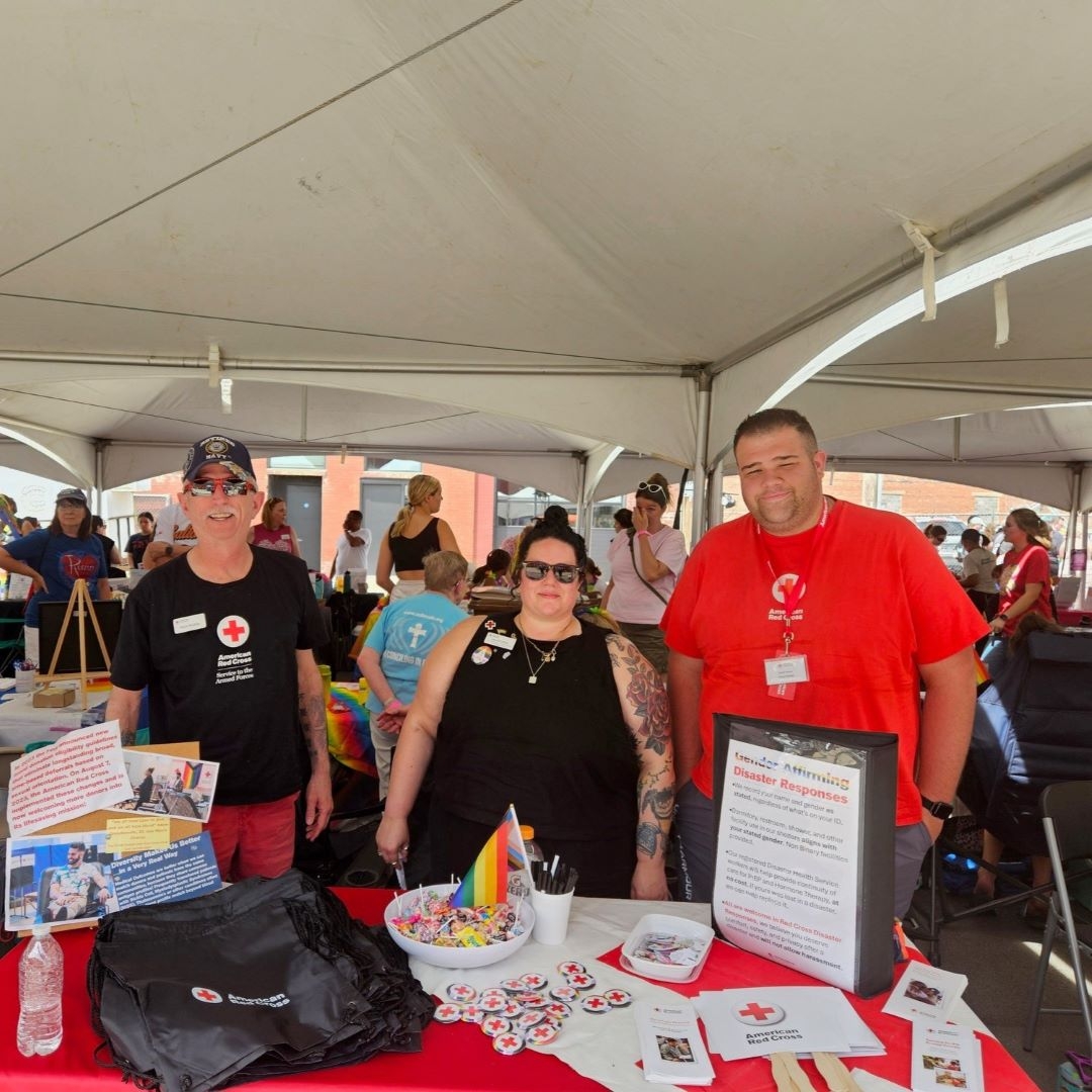 three red cross volunteers stand behind table