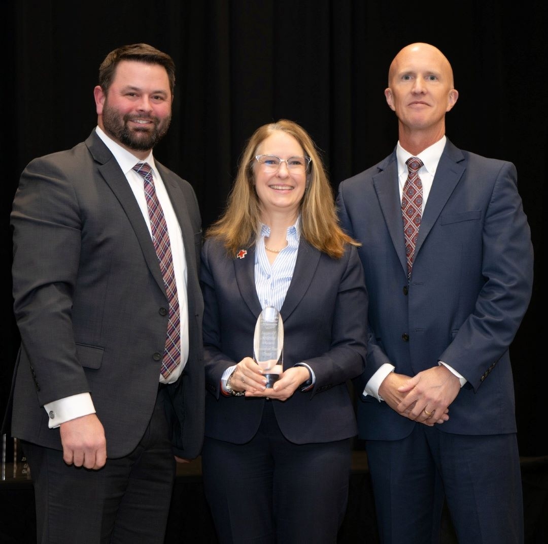 woman in suit holds award while standing between two men