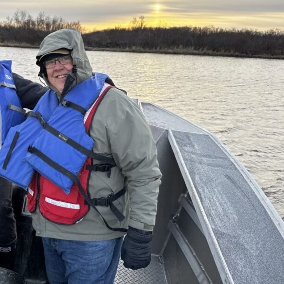 joe on a boat over large lake wearing a red cross vest 