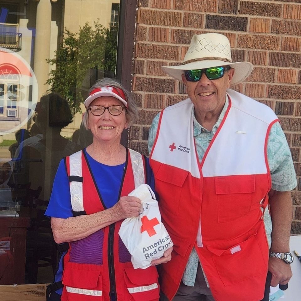 two volunteers wearing red cross vest holding red cross goody bags