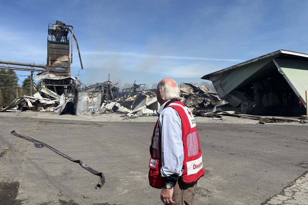Man in Red Cross vest looks out over damaged building