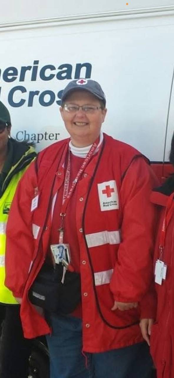 Woman in Red Cross vest stands in front of emergency response vehicle