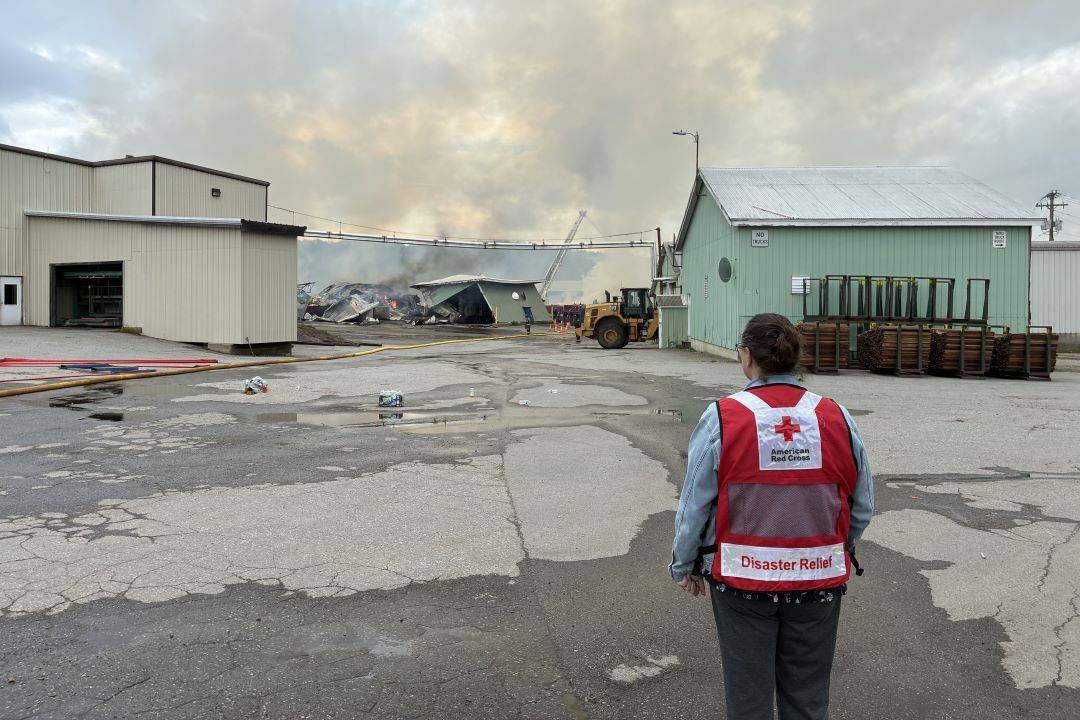 Woman in Red Cross vest looks out over damaged building